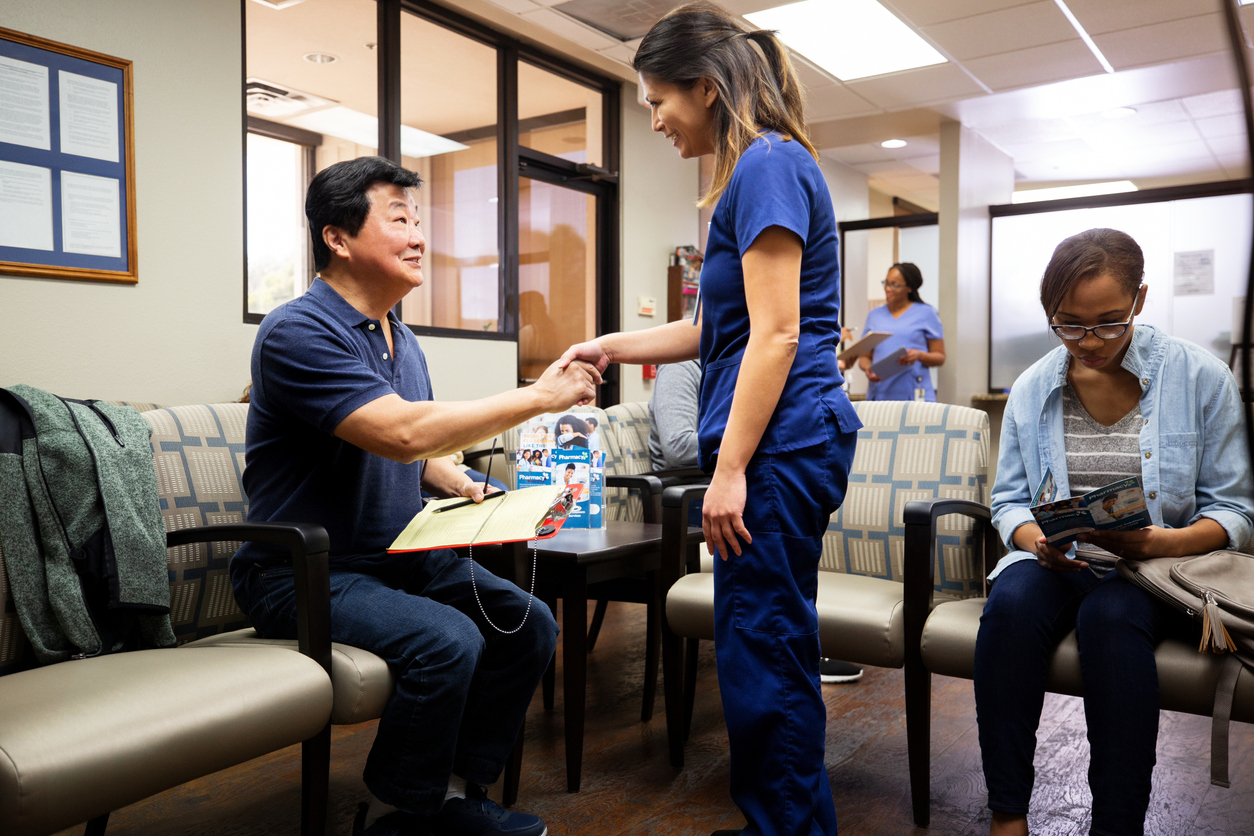 Patient in waiting room shaking hands with medical professional in scrubs